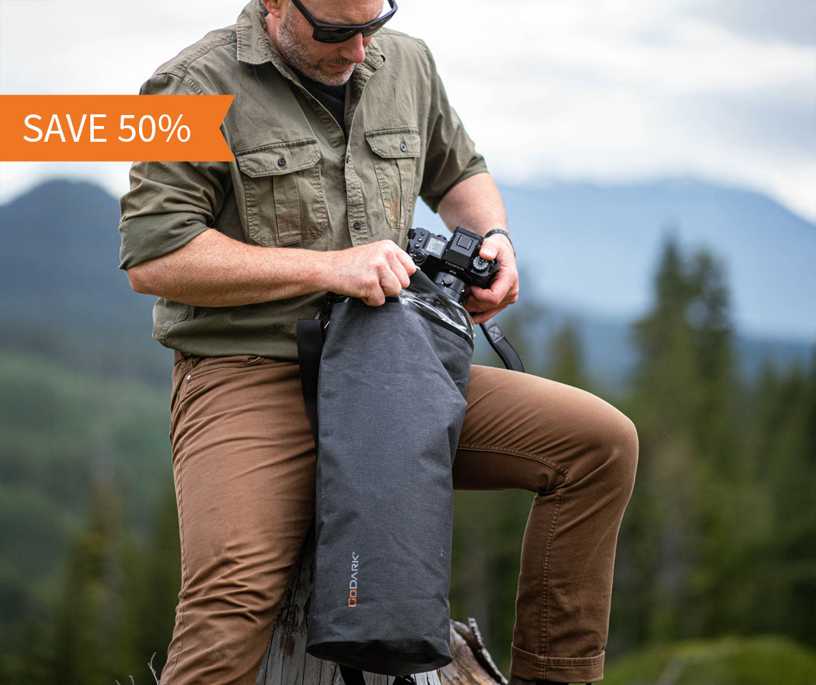 Man in outdoor gear with camera and GoDark Dry Bag against a mountainous background, promotional text 'SAVE 50%' displayed.