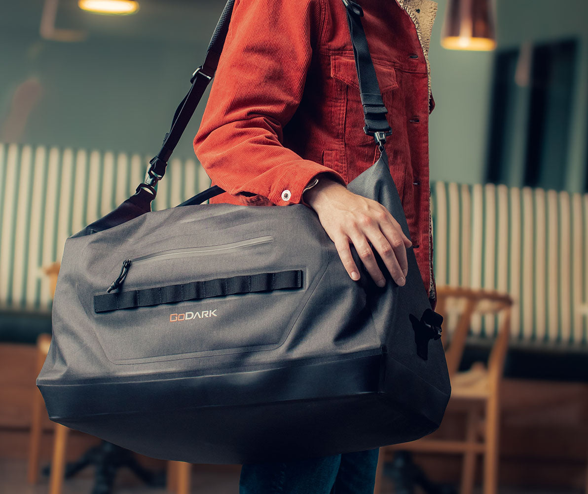 Person holding a gray duffel bag with 'Gadark' branding in an indoor setting.