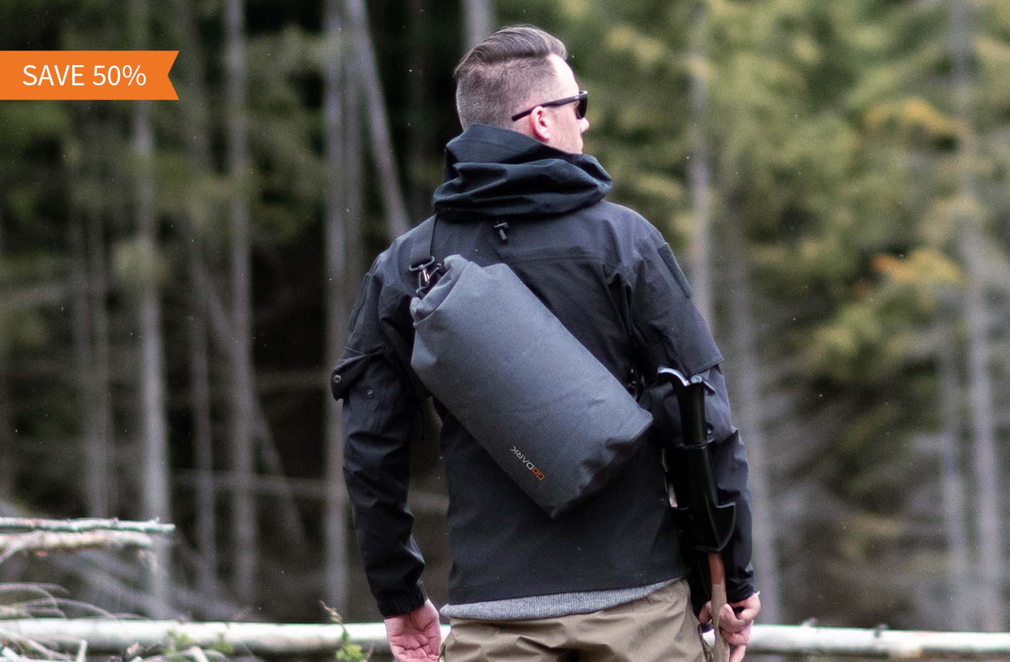 Person wearing a black jacket and carrying a GoDark Dry bag in a forest with a 'SAVE 50%' banner